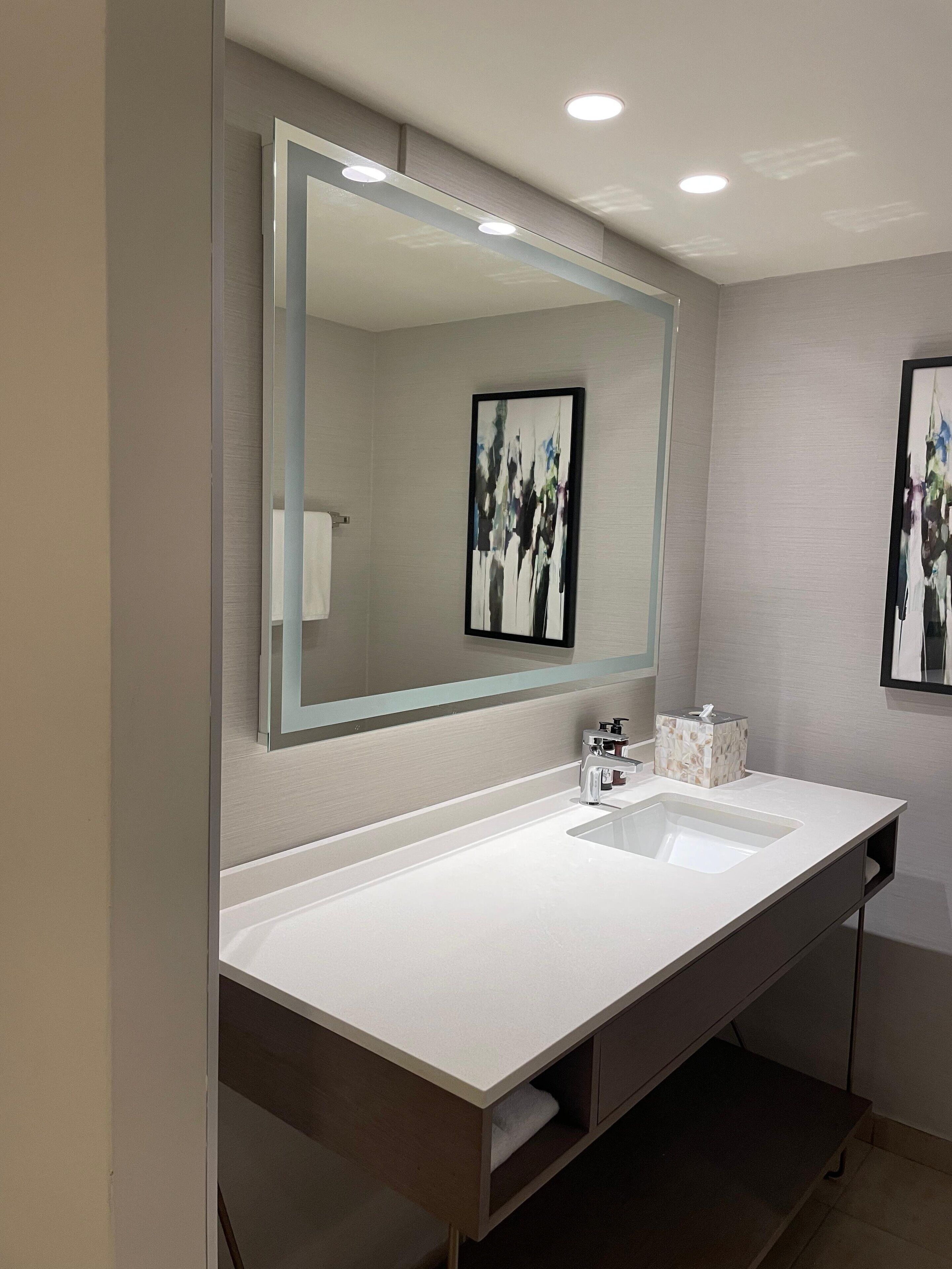 Un baño moderno con un espejo grande, dos lavamanos y un perchero para toallas.