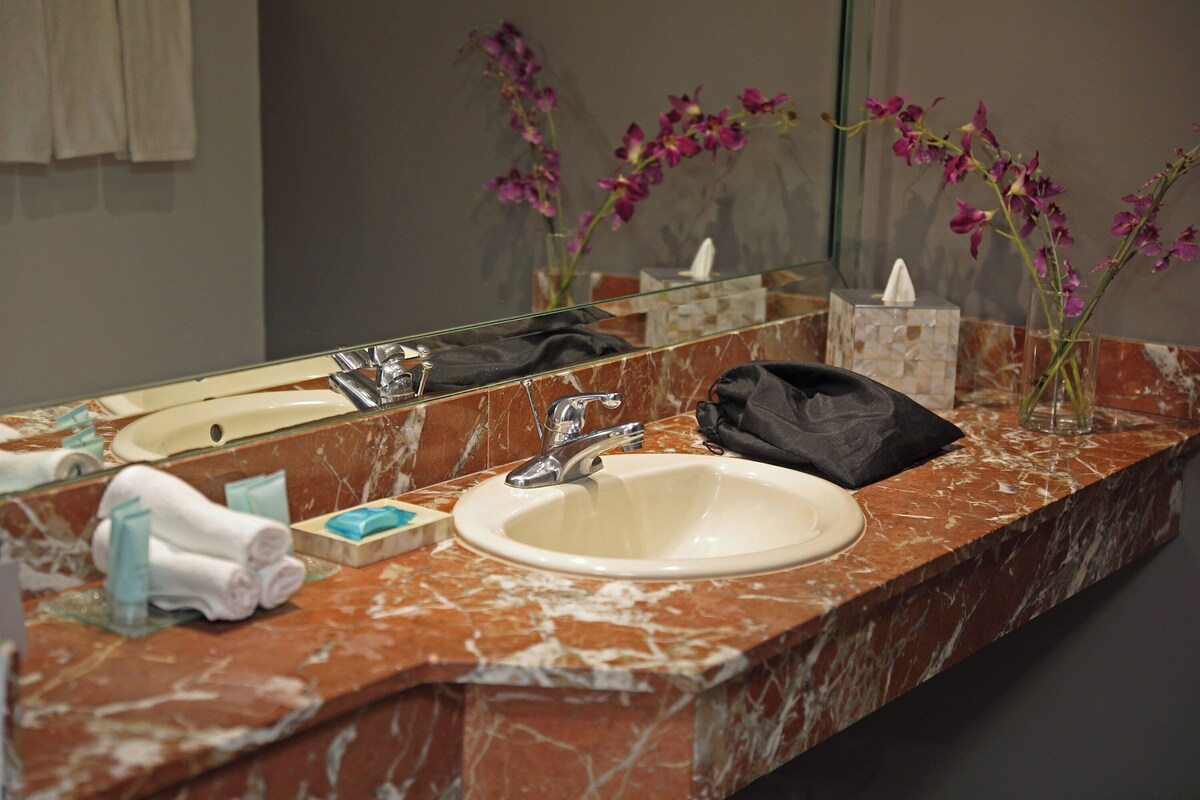 Un baño con lavamanos de mármol, un espejo y un florero con flores.