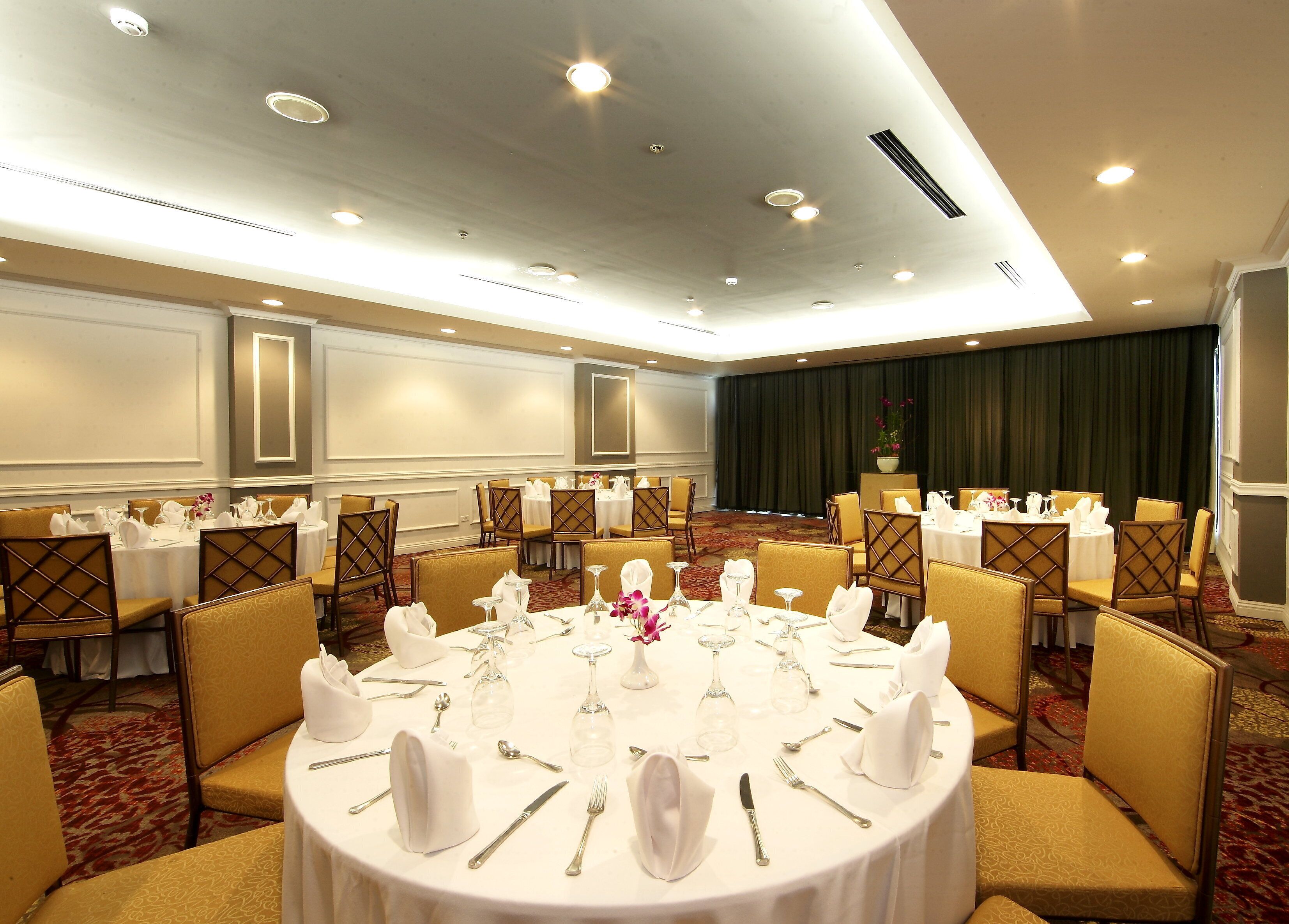 Een feestzaal met ronde tafels gedekt voor een diner, voorzien van witte tafelkleden, stoelen en bestek.