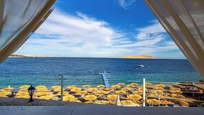 Una playa con sombrillas, un muelle y barcos a lo lejos.