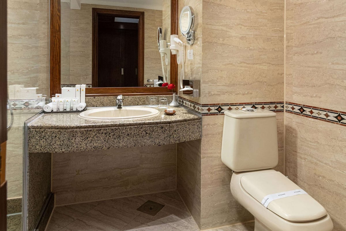 A modern bathroom with a marble sink, a toilet, and a large mirror.