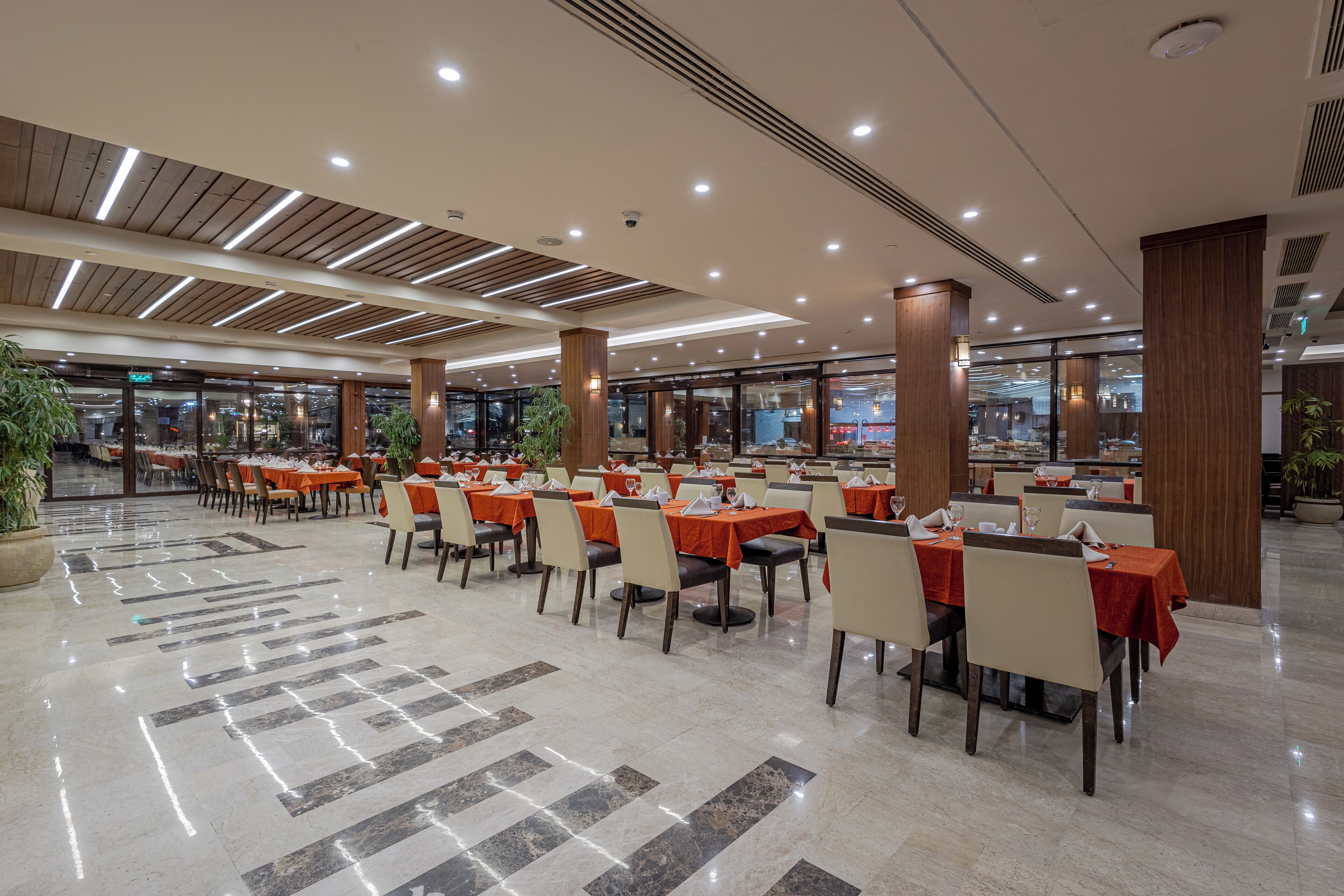 Un vaste espace intérieur aménagé en salle à manger, avec de nombreuses tables et chaises, de grandes colonnes et un sol en marbre poli.