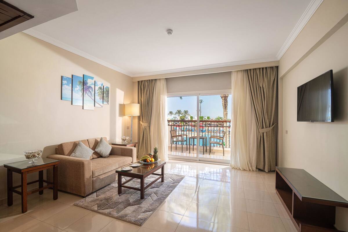A hotel room with a sofa, coffee table, TV, and a balcony with a pool view.