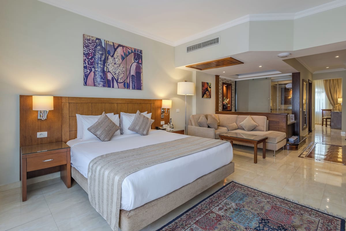 A hotel room with a large bed, a sofa, a desk, and a painting on the wall.