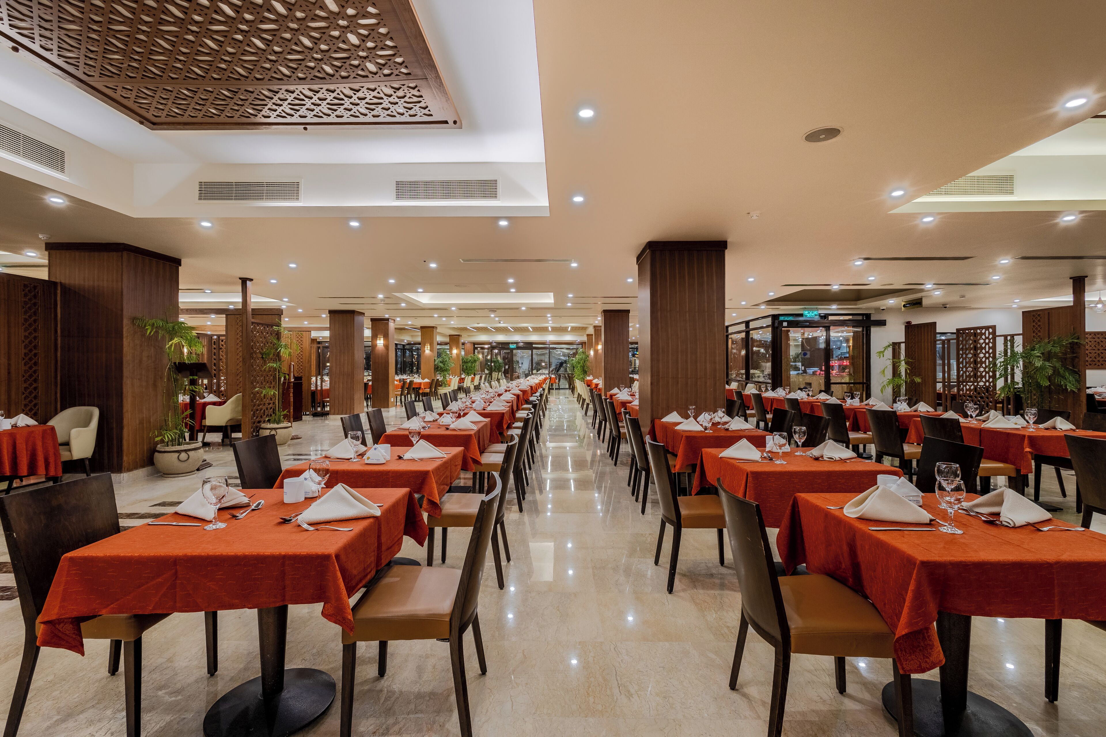 A spacious dining area with multiple tables set for guests, featuring a modern design with wooden accents and a central walkway.