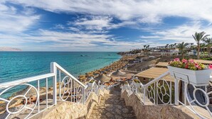 Un hôtel en bord de mer, doté d’un escalier en pierre menant à une plage aménagée avec des parasols et des chaises longues.