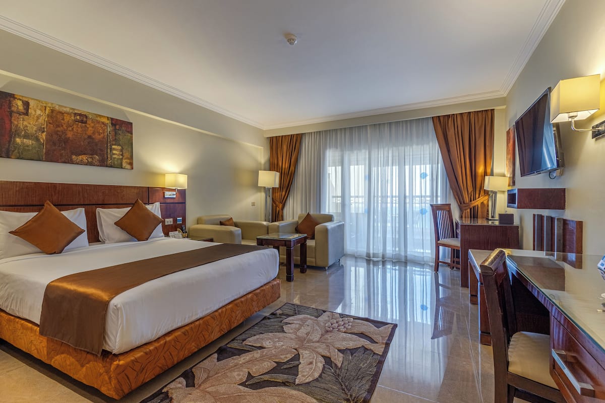A hotel room with a large bed, a desk, a chair, a sofa, and a television.