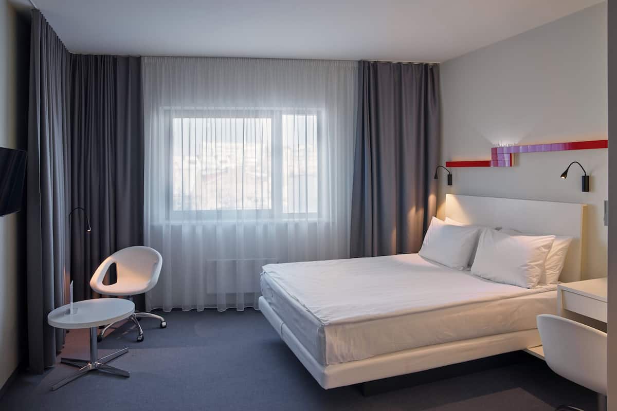 A modern hotel room with a large bed, a desk, a chair, and a TV.