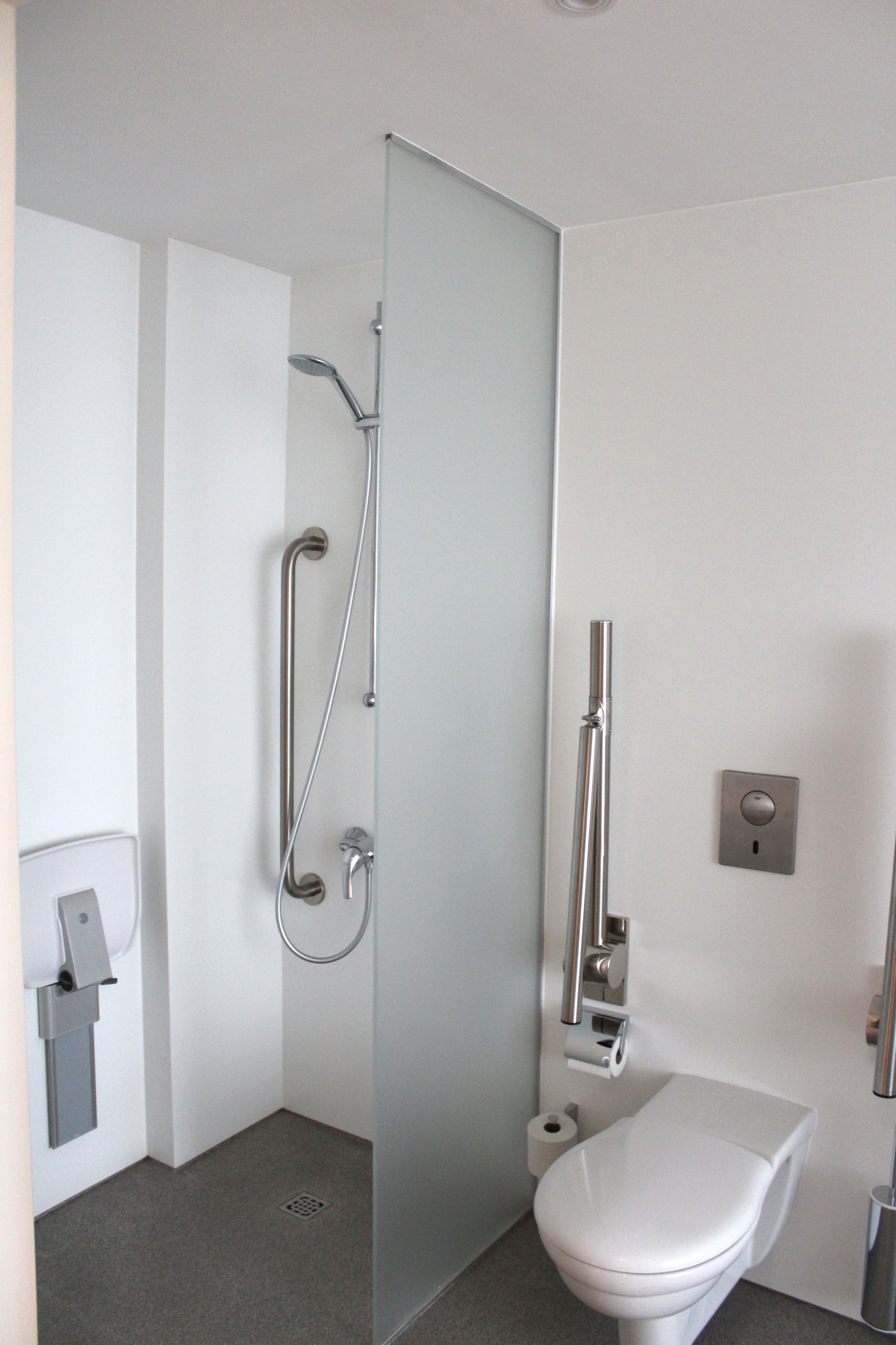 Et moderne badeværelse med toilet, brusekabine i glas og håndtørrer.