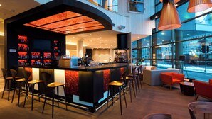 A modern bar area with a curved counter, multiple stools, and a seating area with orange chairs. - Holiday Inn Vilnius by IHG (Vilnius)