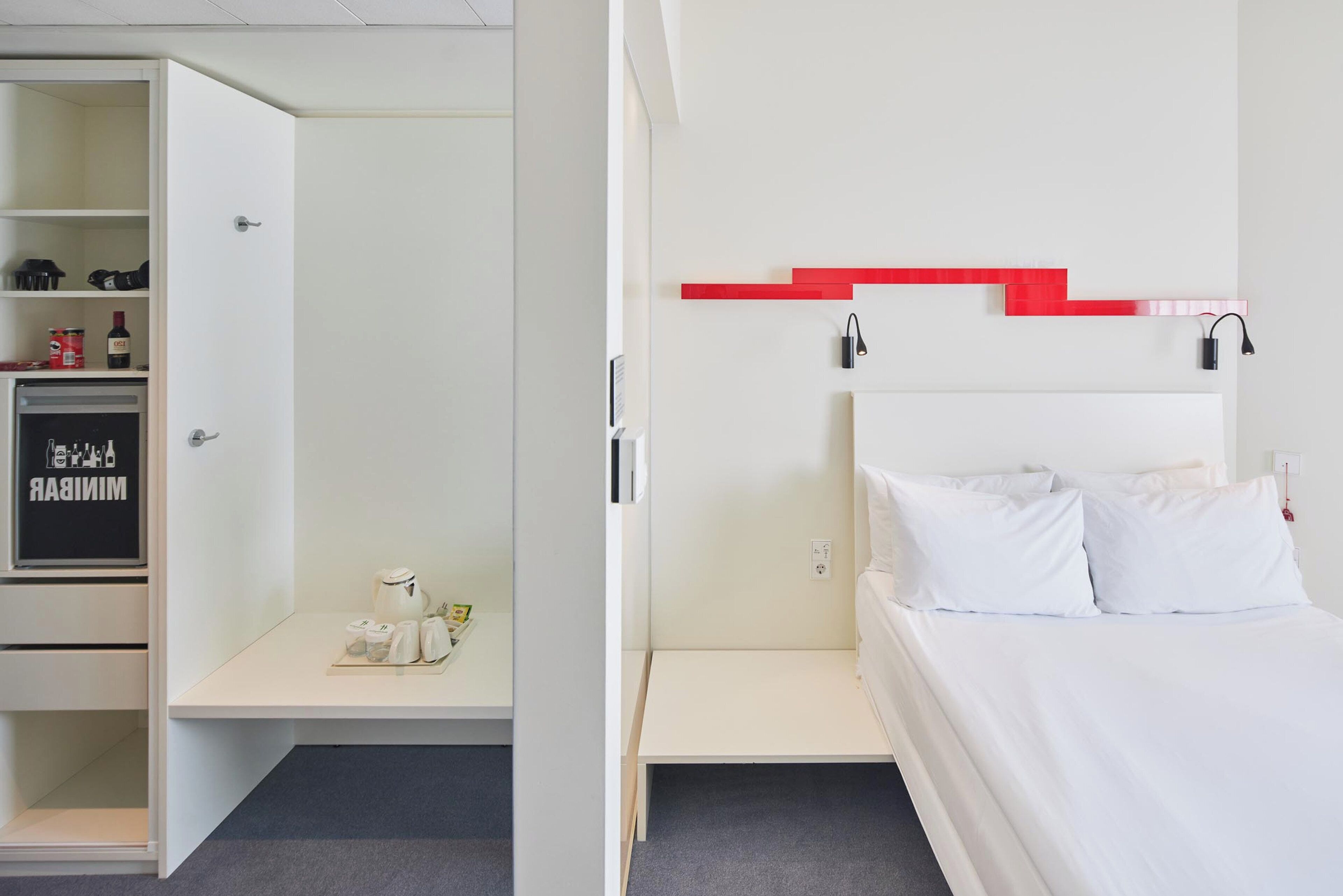 Habitación de hotel con cama, armario blanco y pared decorada en rojo.