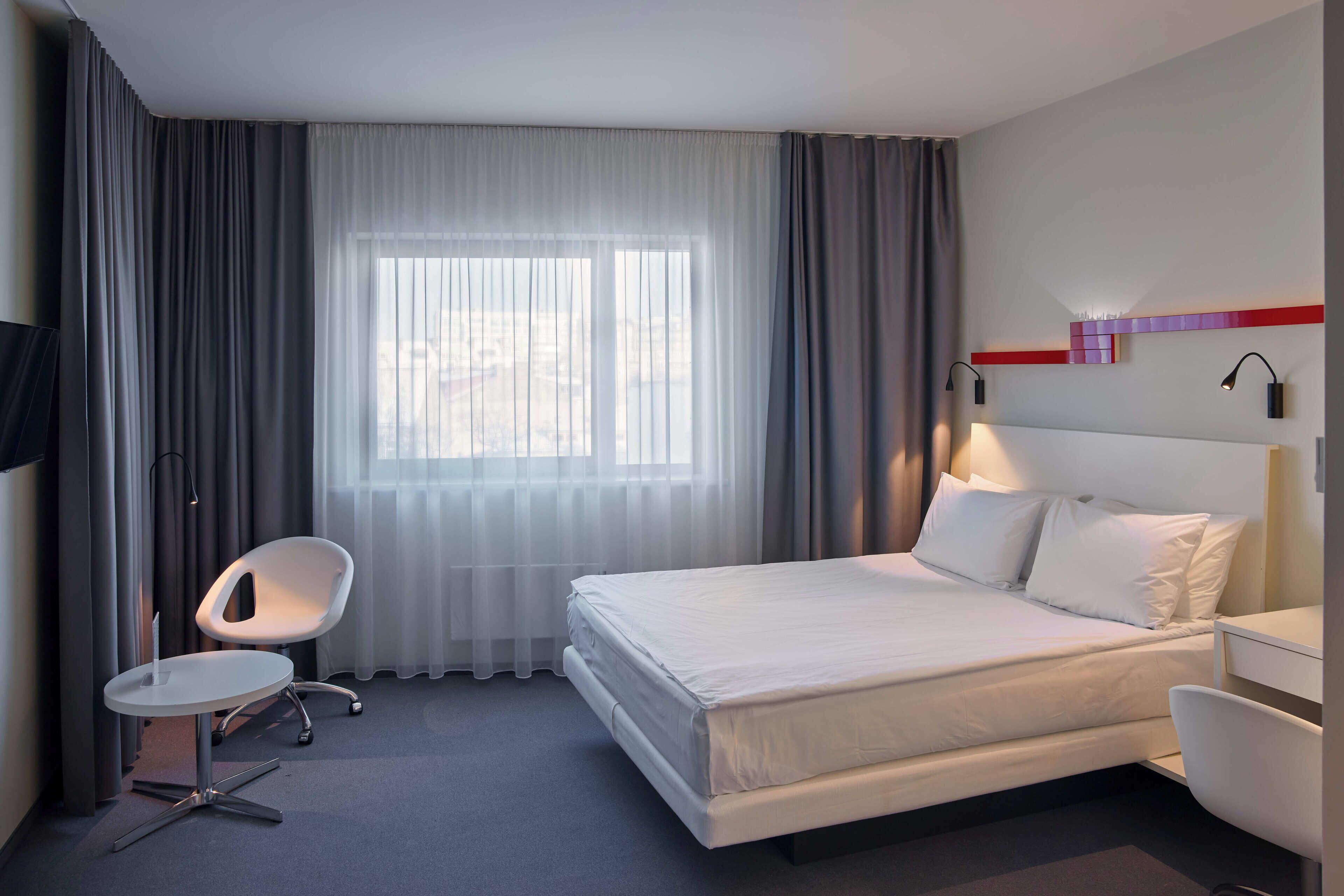 Una habitación de hotel moderna con una cama grande, un escritorio, una silla y un televisor.