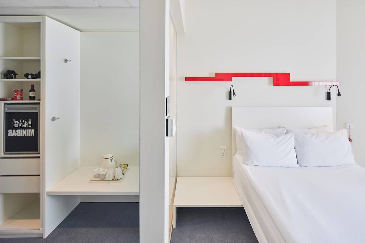A hotel room with a bed, a white wardrobe, and a red accent wall.