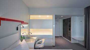 Una habitación de hotel moderna con cama, escritorio, silla, minibar y vestidor.
