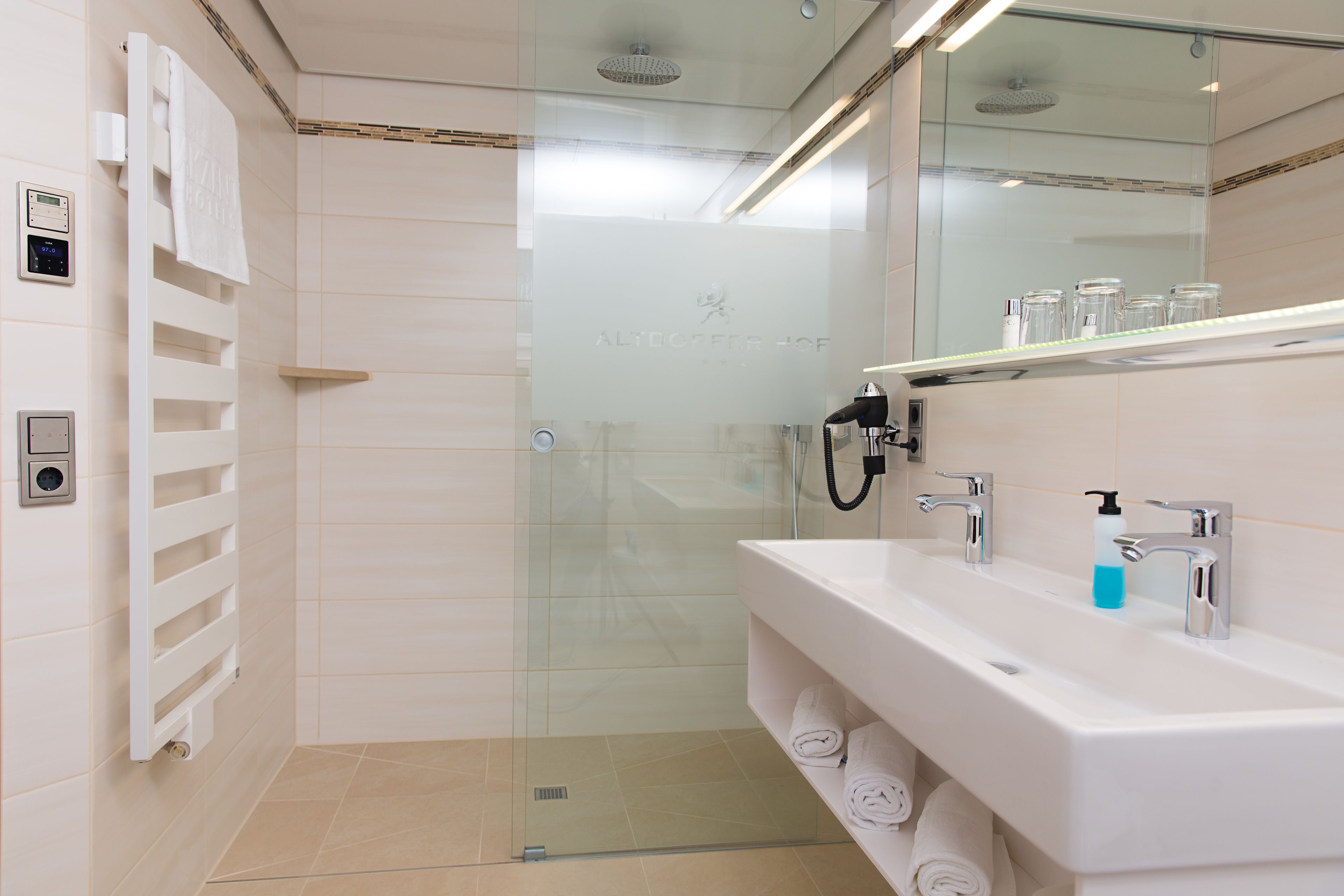 A modern bathroom with a glass shower enclosure, a white sink with two faucets, and a towel rack with folded towels.