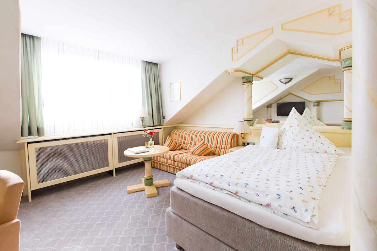 A hotel room with a bed, a sofa, a small table, and a window with curtains.