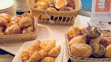 Una mesa de buffet con panes y pasteles varios, incluyendo croissants y bollos, dispuestos en platos y cestas.