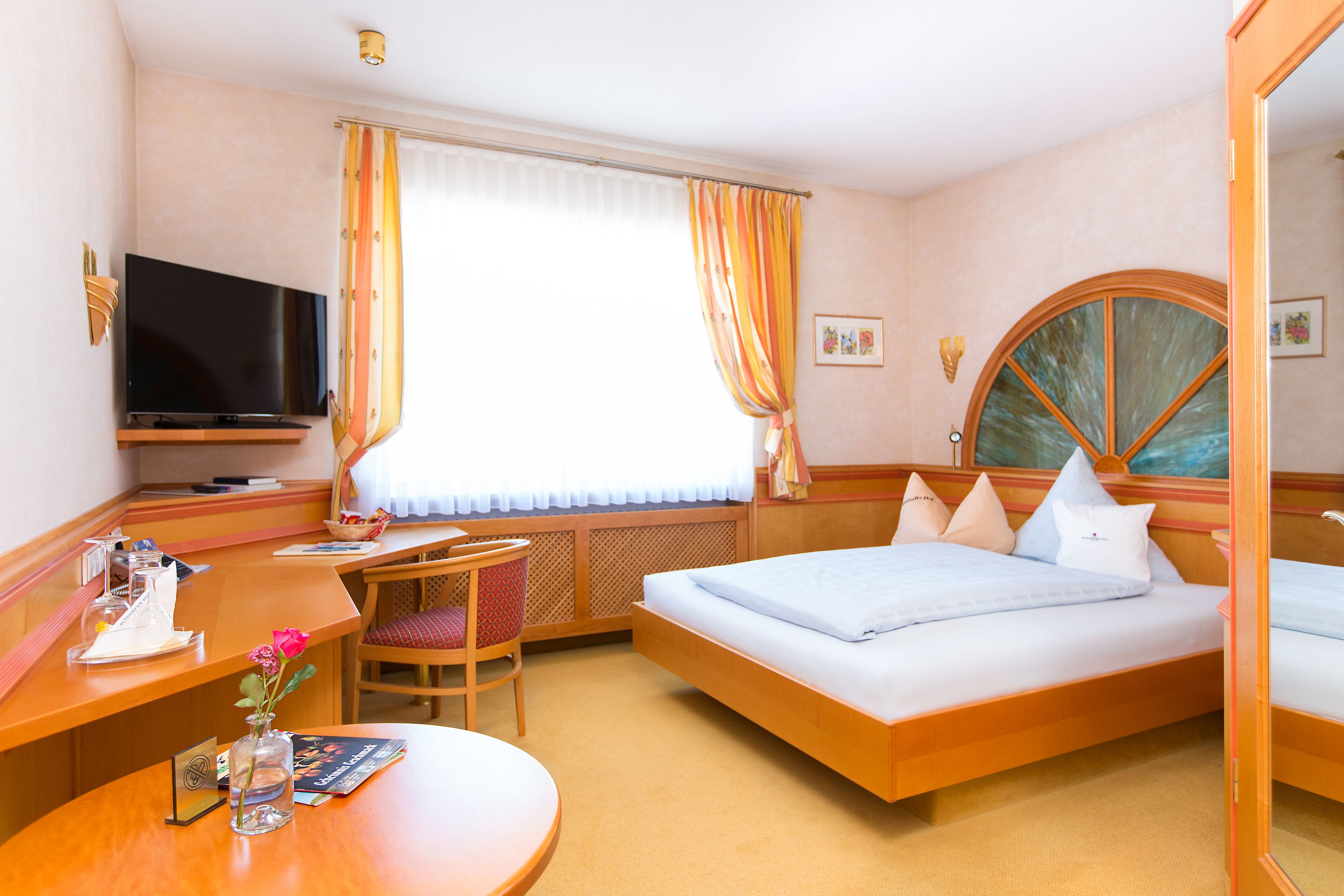 A hotel room with a bed, a desk, a chair, a TV, and a window with curtains.