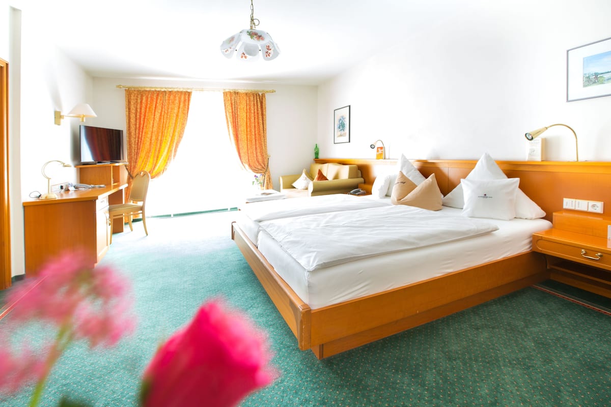 A hotel room with a large bed, a desk with a computer, a television, and a window with curtains.