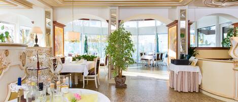 A luxurious dining area with ornate furniture, a central potted plant, and a view through an arched doorway.