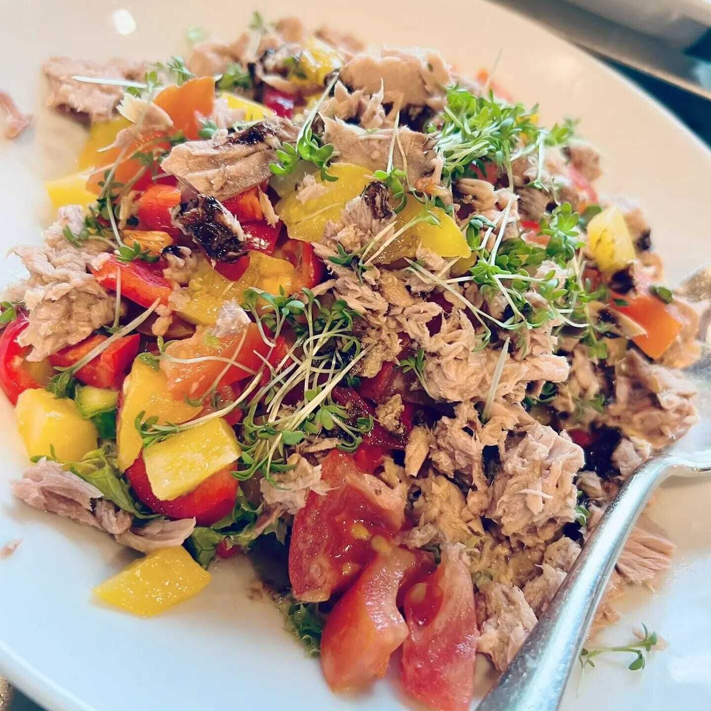 A plate of shredded chicken salad with mixed vegetables and sprouts.