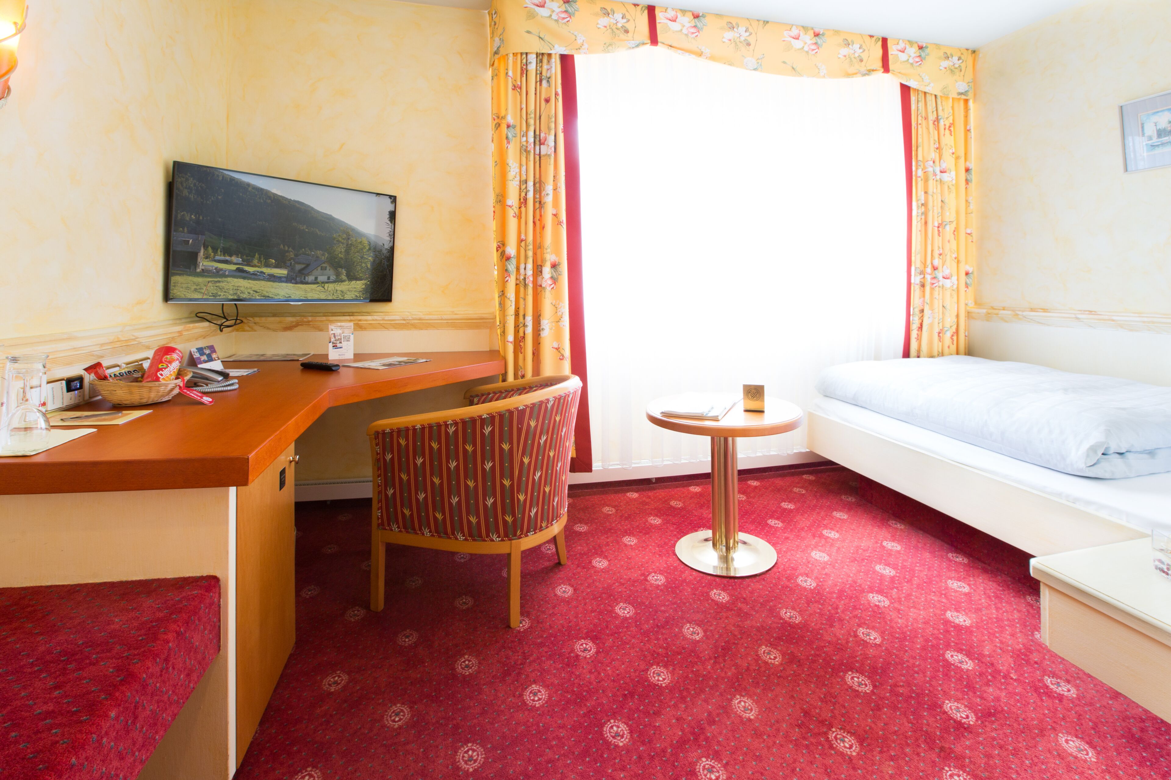 Ein Hotelzimmer mit Bett, Schreibtisch mit Fernseher, Stuhl und kleinem Tisch.