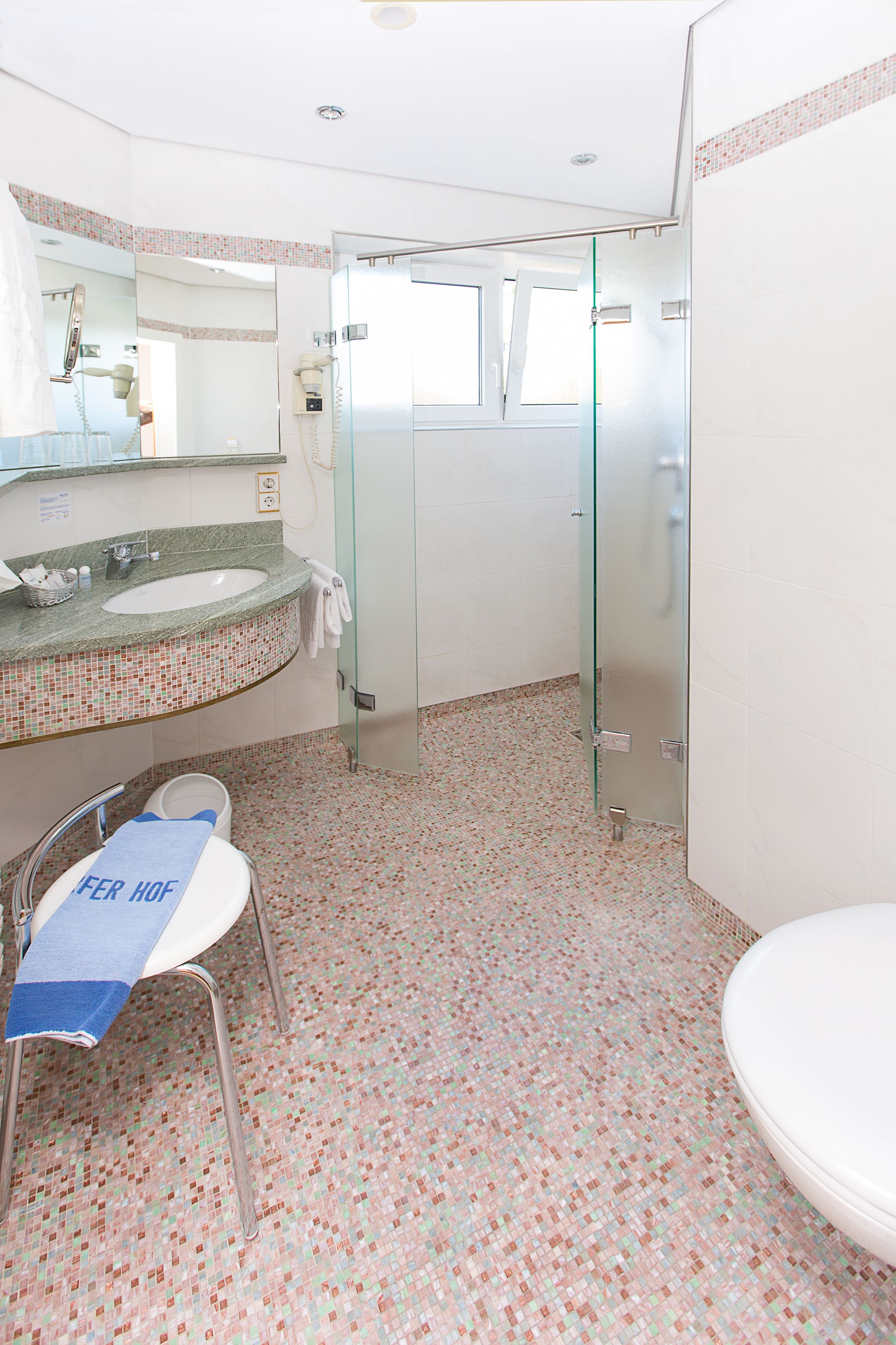 A bathroom with a glass shower enclosure, a sink with a mosaic tile backsplash, and a toilet with a towel on the seat.