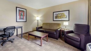 A hotel room with a sofa, a desk with a chair, a coffee table, and two lamps.