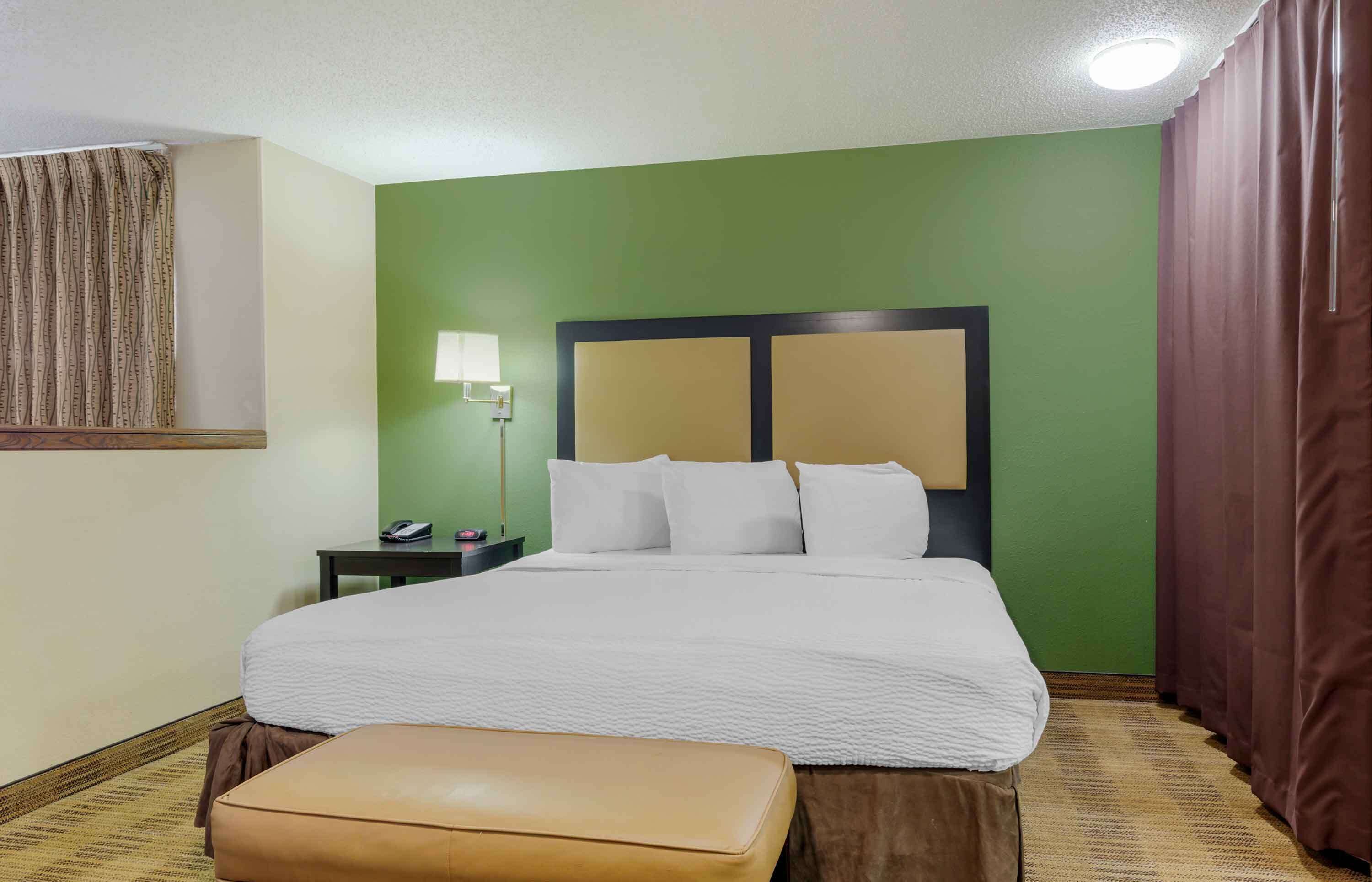 A hotel room with a large bed, a bedside table, a lamp, and a curtain.
