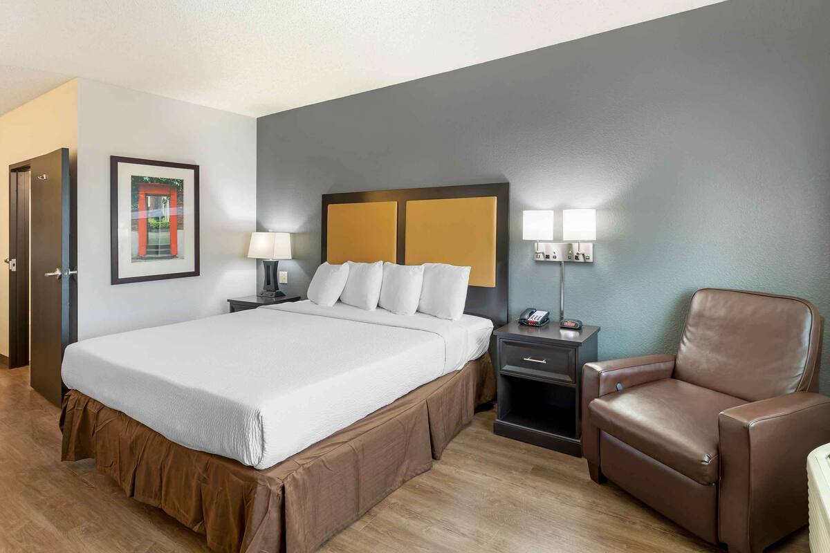 A hotel room with a large bed, two bedside tables with lamps, a brown leather chair, and a framed picture on the wall.