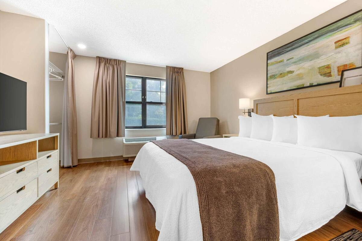 Een hotelkamer met een groot bed, een televisie, een bureau en een raam met gordijnen.