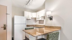 A compact kitchen with white cabinets, a microwave, a refrigerator, and a small dining area with a bench.
