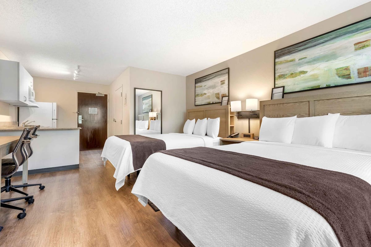 Hotelkamer met twee bedden, een bureau en een stoel. Er hangt een schilderij aan de muur en een deur die naar een andere kamer leidt.