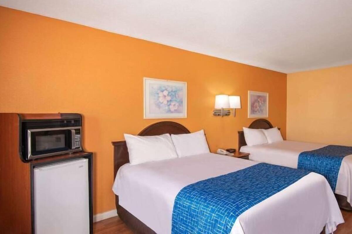 A hotel room with two beds, a microwave, a small refrigerator, and two wall-mounted lamps.