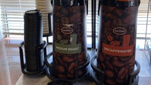 Duas máquinas de café identificadas como 'Medium Roast' e 'Descafeinado' da Farmer Brothers, com cápsulas de café e uma máquina de waffles em uma bancada.