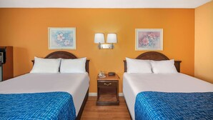 Quarto de hotel com duas camas, uma mesa de cabeceira com telefone e relógio, e duas luminárias fixadas na parede.