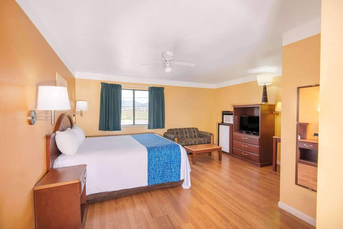 A hotel room with a bed, a TV, a desk, a chair, a ceiling fan, and a window with curtains.