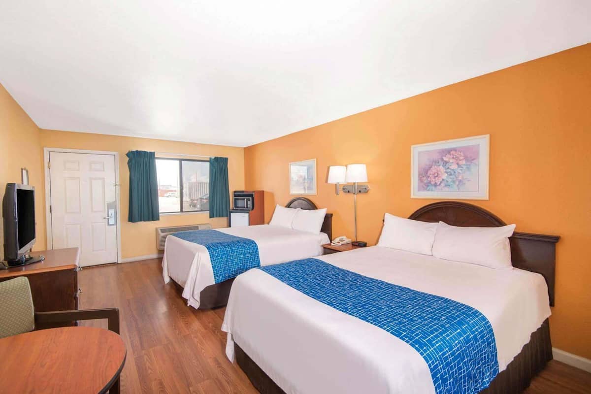 A hotel room with two beds, a desk, a television, and a window with curtains.