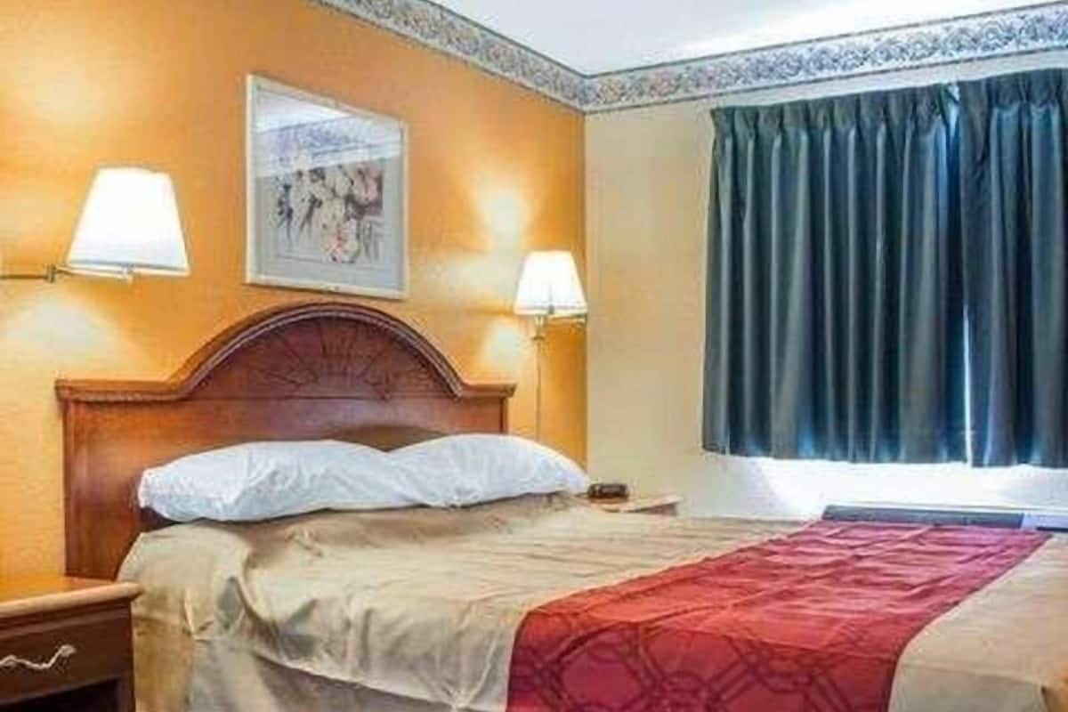 A hotel room with a bed, two bedside lamps, a window with curtains, and a framed picture on the wall.
