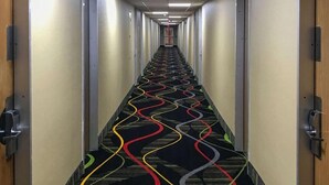 Un largo y estrecho pasillo de hotel con alfombra estampada y puertas a ambos lados.