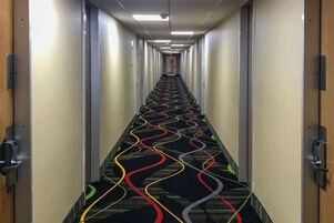 Un largo y estrecho pasillo de hotel con alfombra estampada y puertas a ambos lados.