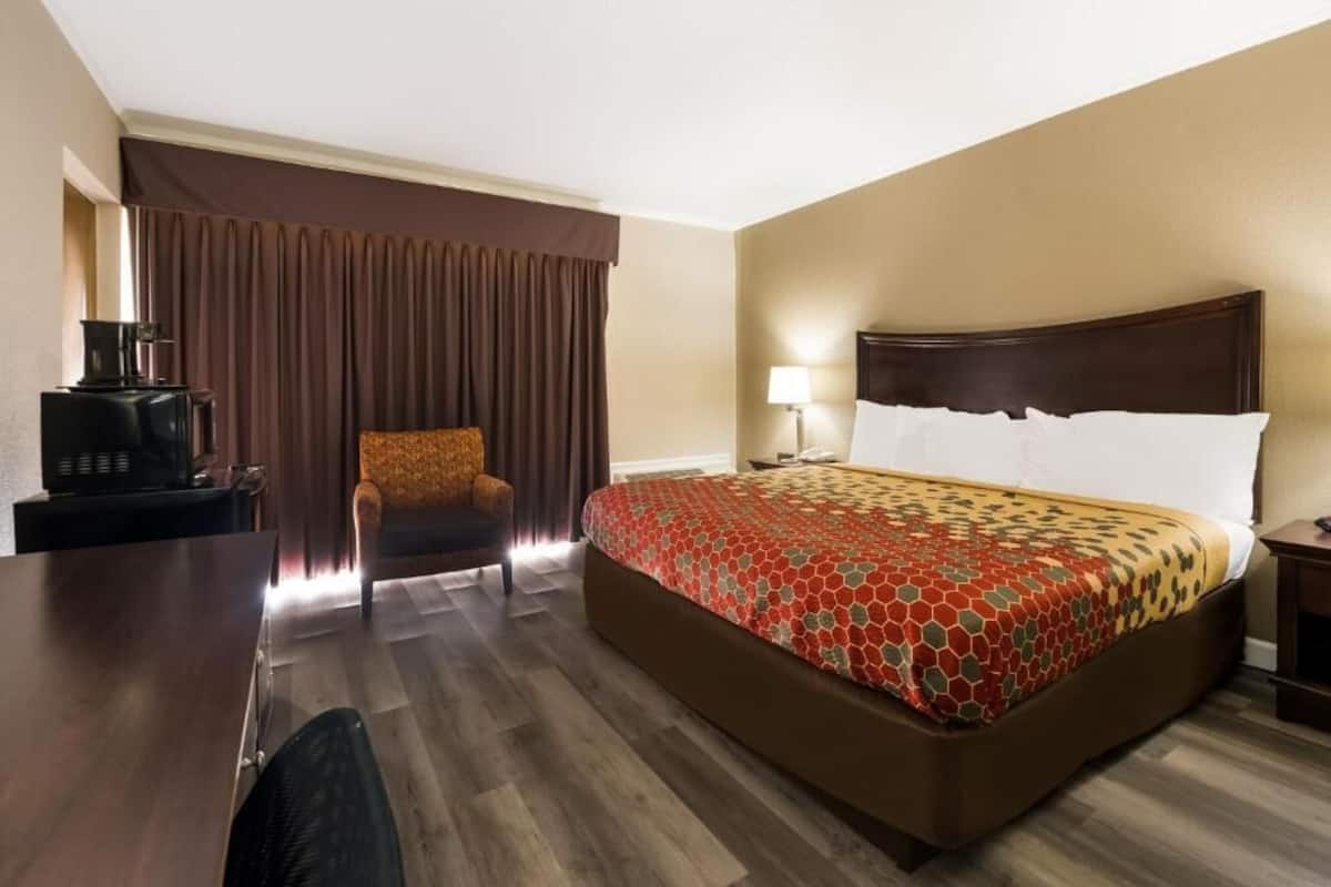 A hotel room with a large bed, a desk with a coffee maker, a chair, and a lamp.