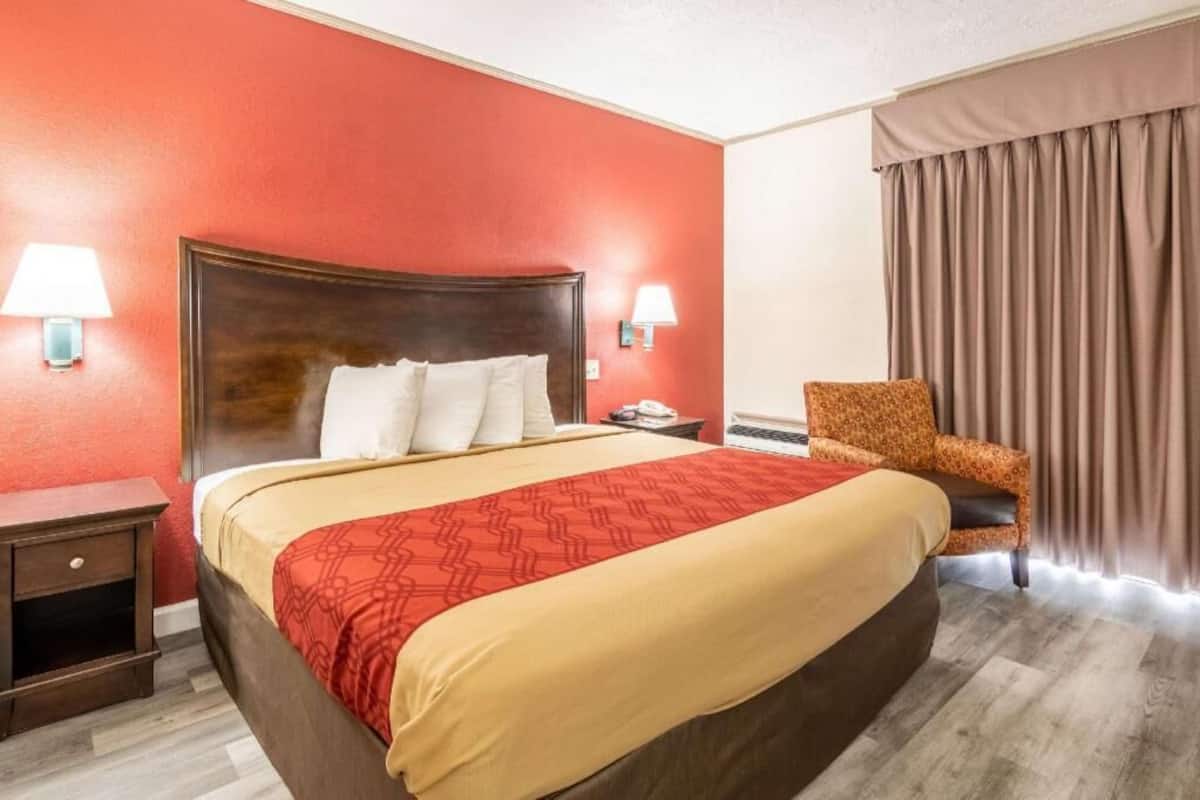 A hotel room with a large bed, two bedside lamps, a chair, and a window with curtains.