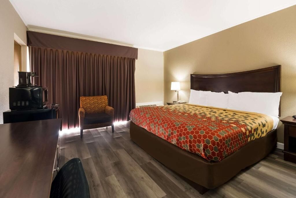 A hotel room with a large bed, a desk with a coffee maker, a chair, and a lamp.