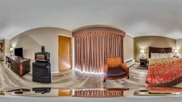 Une chambre d’hôtel avec un plafond incurvé, un lit recouvert d’une courtepointe à motifs, un bureau avec un ordinateur et une télévision, et une chaise.