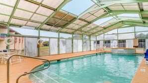 Una piscina interior con techo de vidrio, un trampolín y una pequeña zona de estar con sillas.