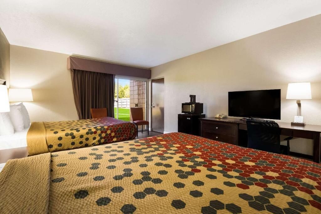 Ein Hotelzimmer mit zwei Betten, einem Schreibtisch, einem Fernseher und einem Sessel.