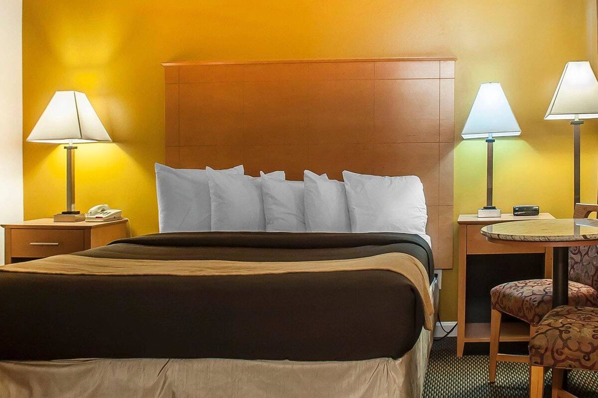 A hotel room with a large bed, two bedside tables with lamps, a small desk with a chair, and a round table with a chair.