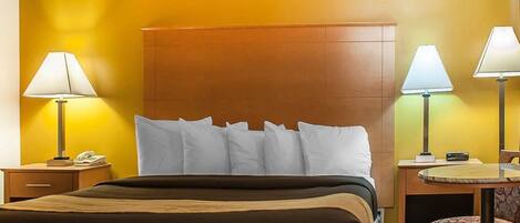 A hotel room with a large bed, two bedside tables with lamps, a small desk with a chair, and a round table with a chair.