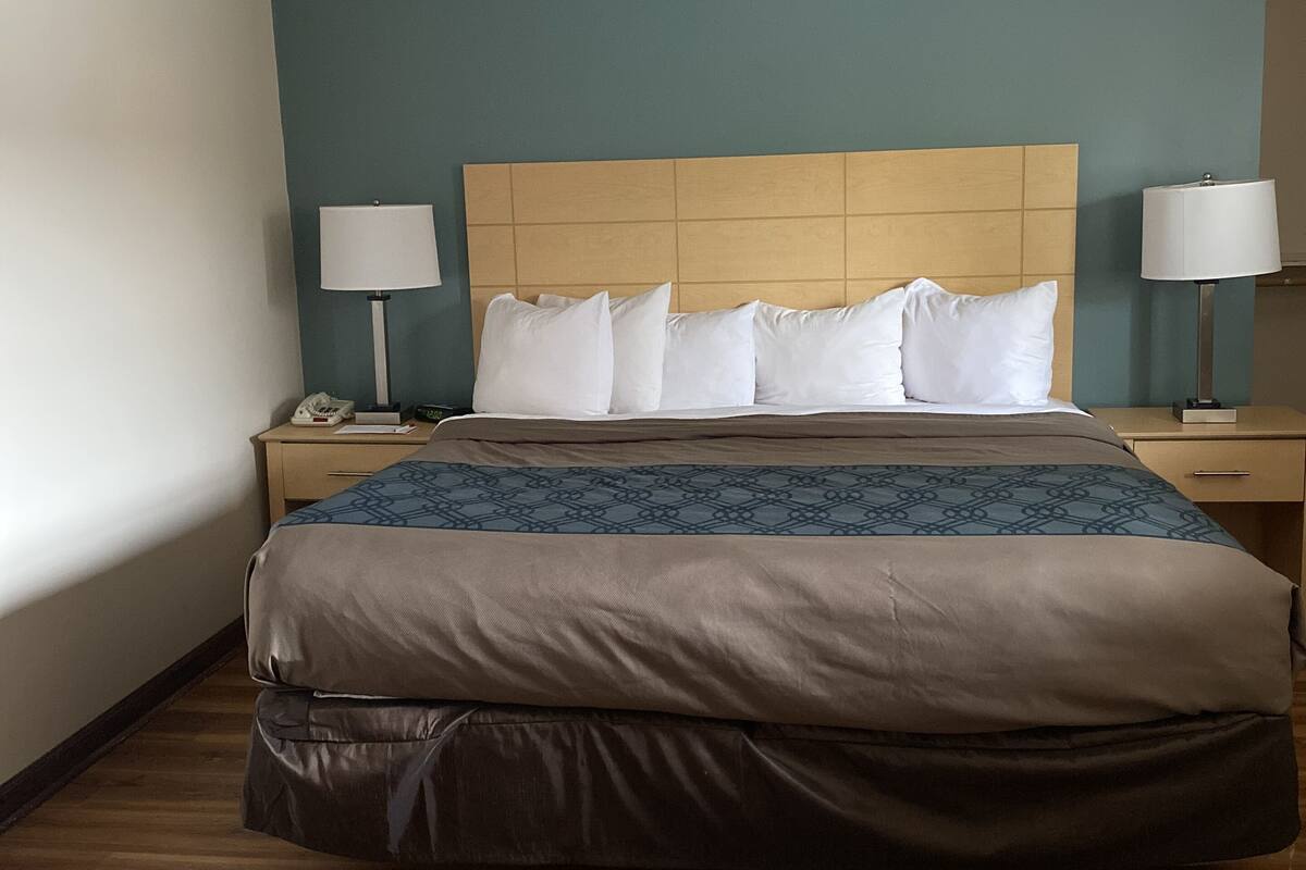 A hotel room with a bed, two bedside tables, a nightstand, a lamp, and a wall clock.